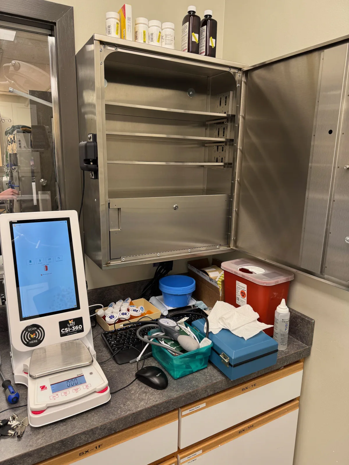 CSI-360 touchscreen and digital scale on a clinic countertop beside an open stainless-steel cabinet