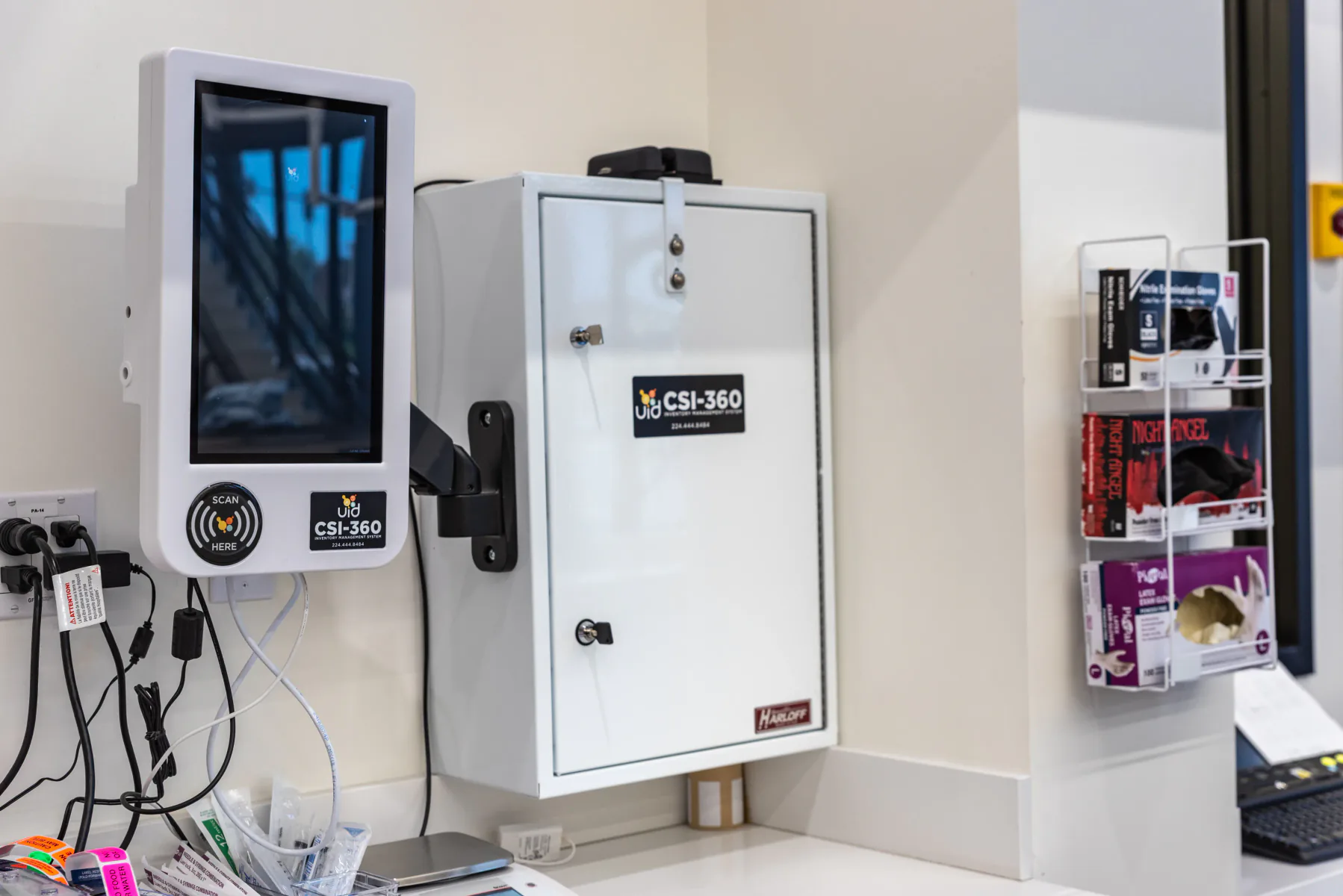 Wall-mounted CSI-360 touchscreen beside a white controlled-substance cabinet above a clinic countertop